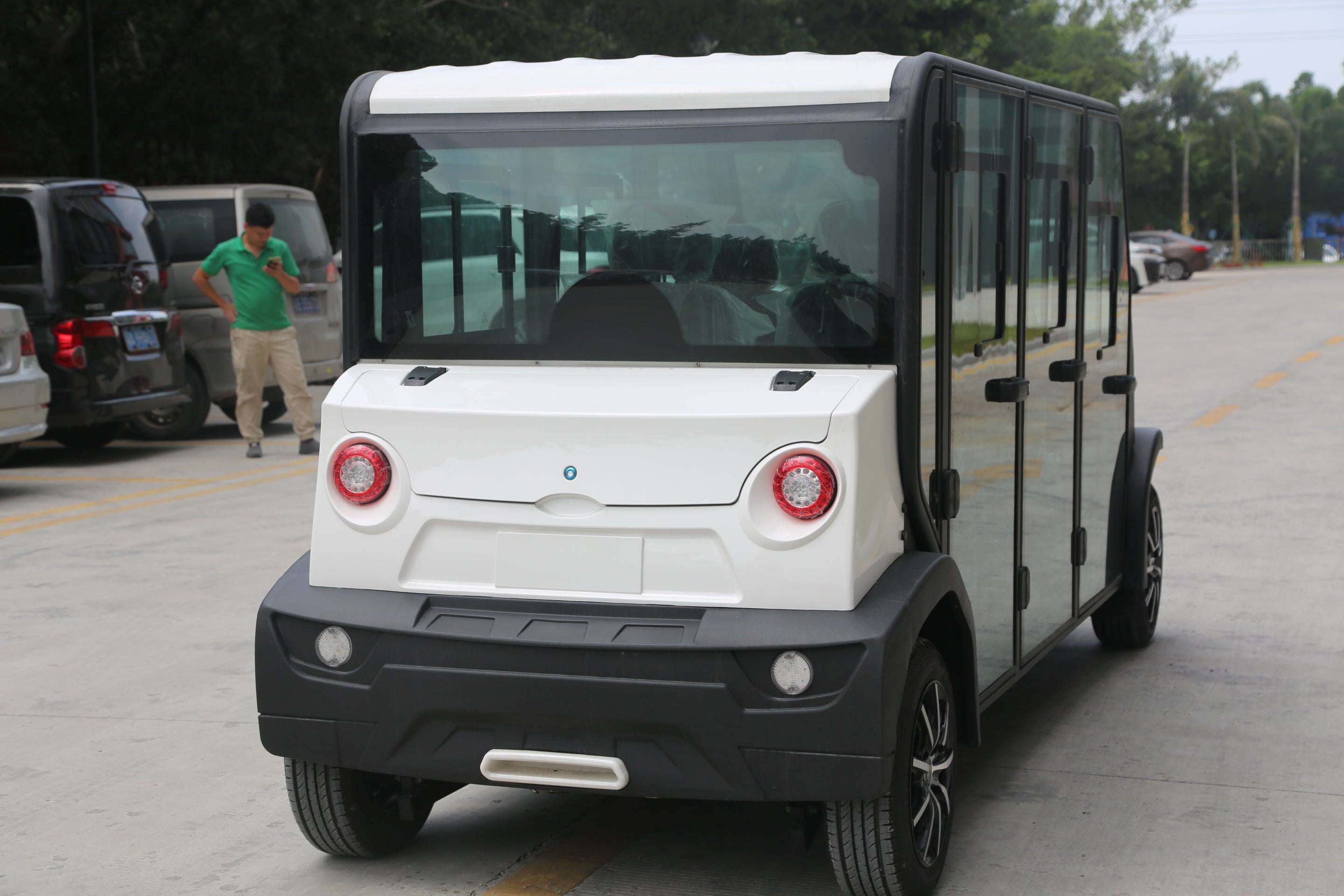 Small electric vehicle on a road with trees and parked cars in the background