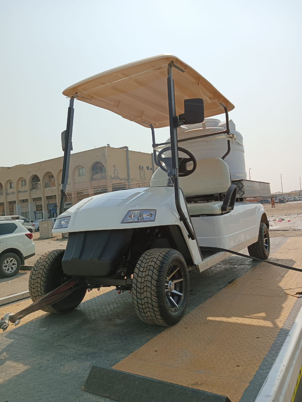 White golf cart with a canopy on a paved area with buildings in the background