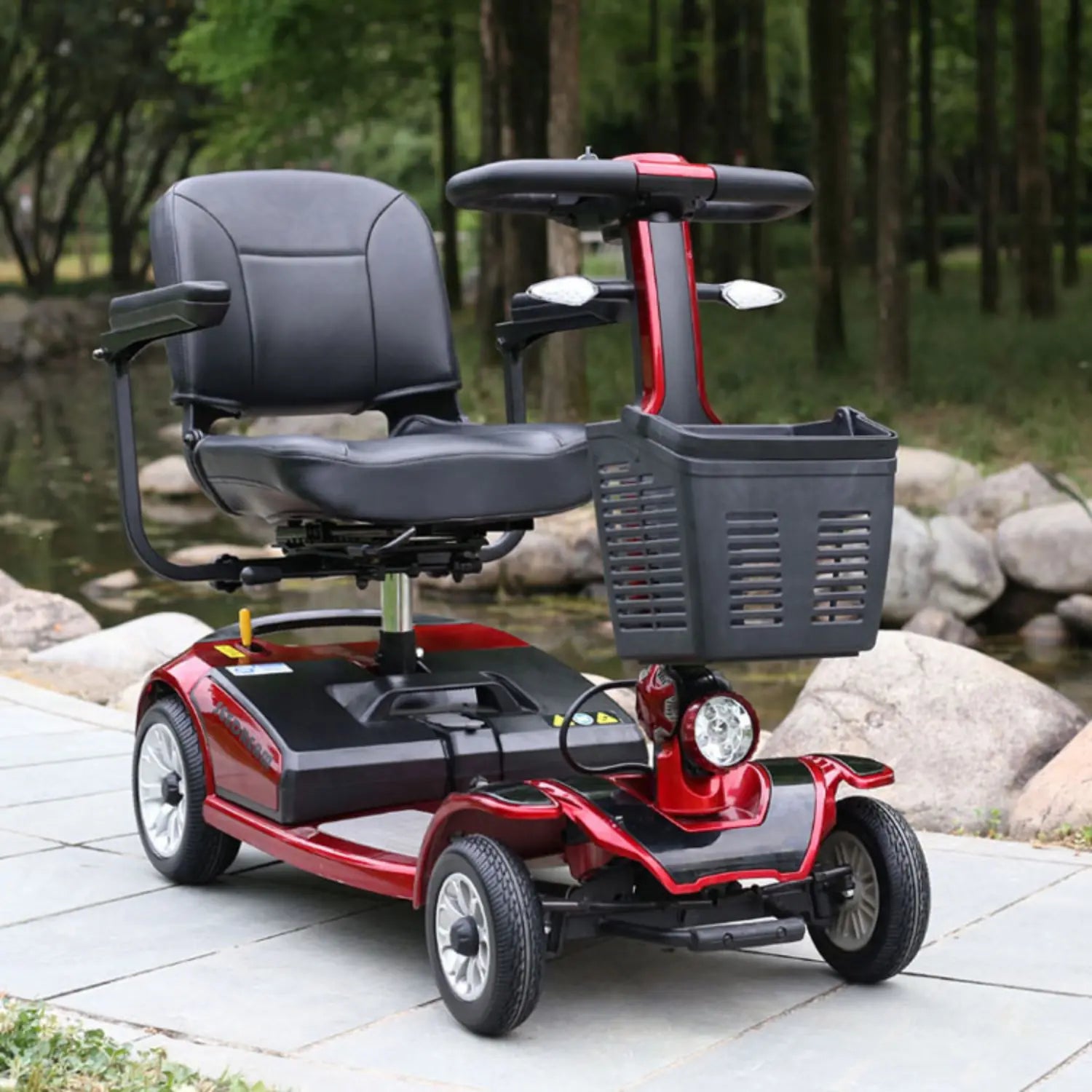 Red and black mobility scooter with a basket on a paved area with a natural background.