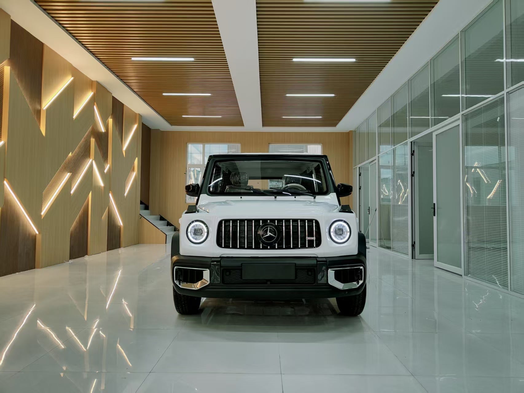 White Mercedes-Benz G-Class SUV in a modern showroom with wooden and glass walls.