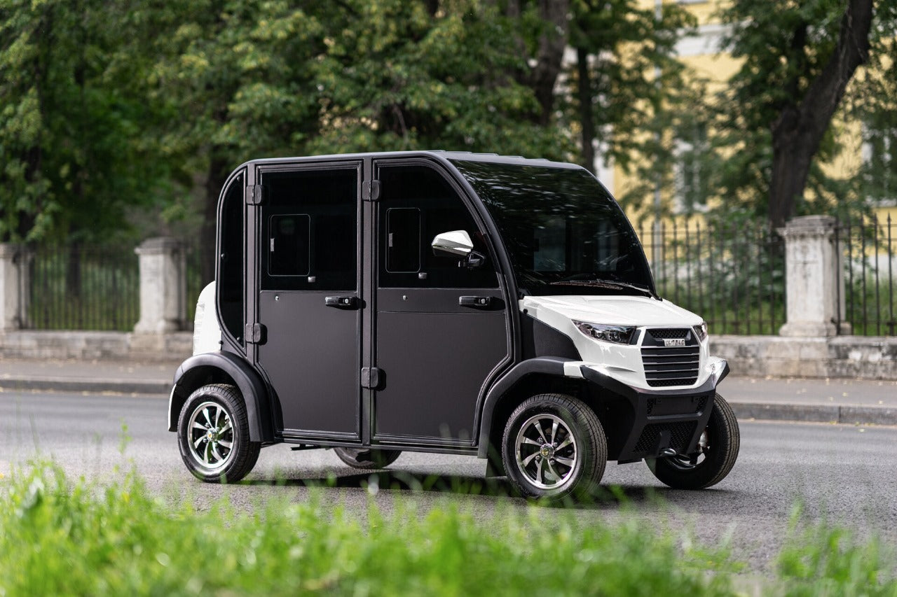 Small electric vehicle on a road with trees and a building in the background