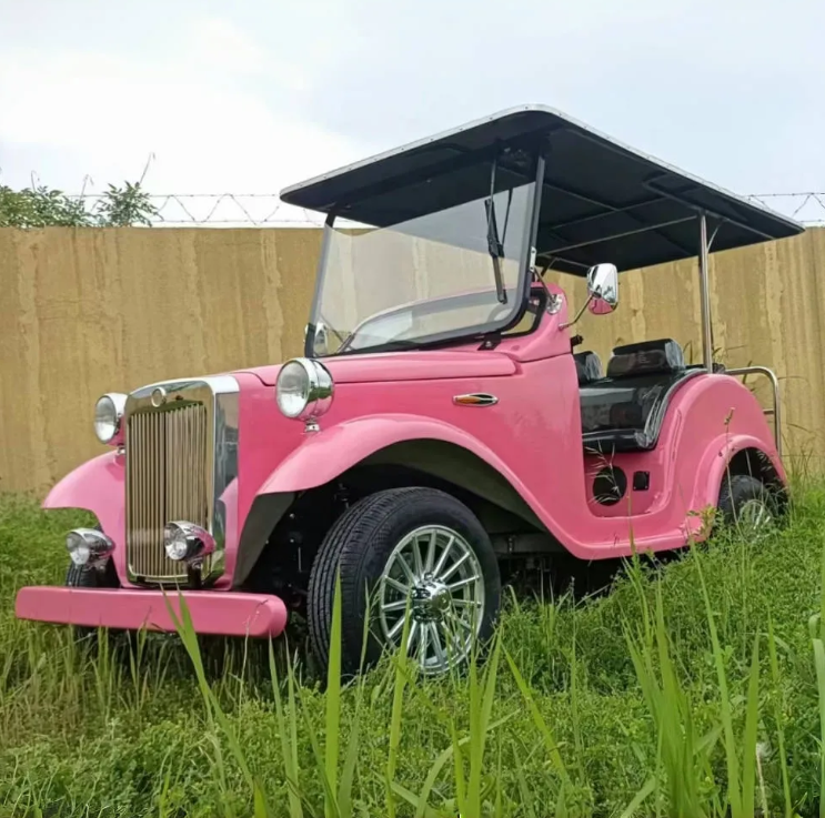 Pink vintage-style golf cart in a grassy area with a wooden fence in the background.