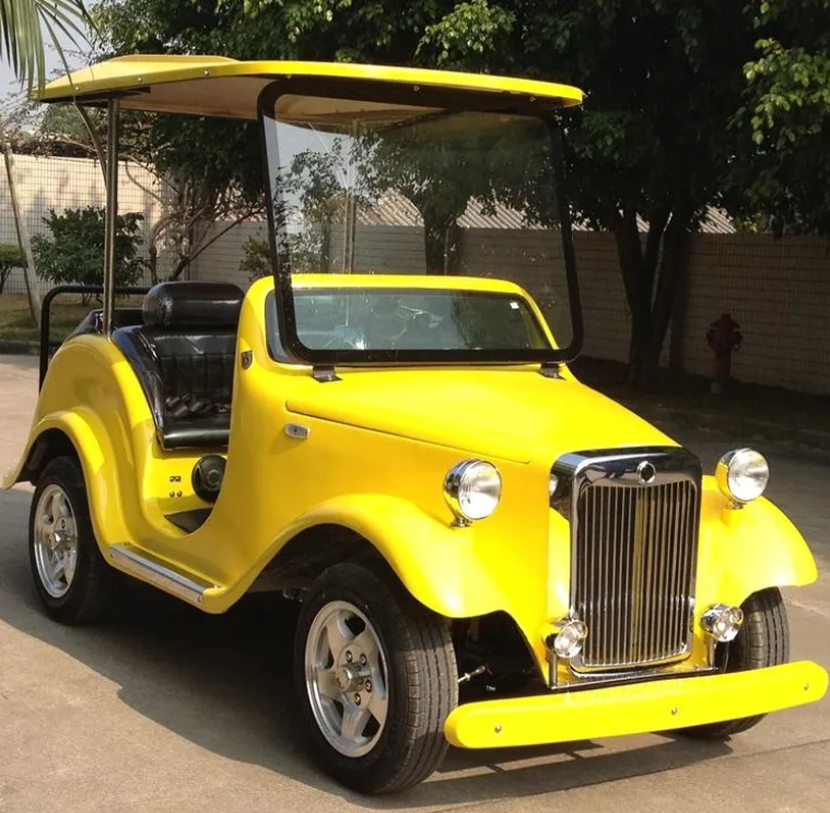 Yellow golf cart on a paved surface with trees and a building in the background