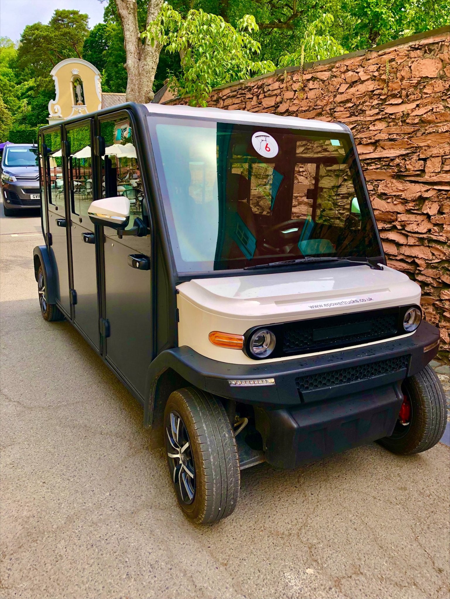 Electric golf cart on a paved path with a stone wall and greenery in the background