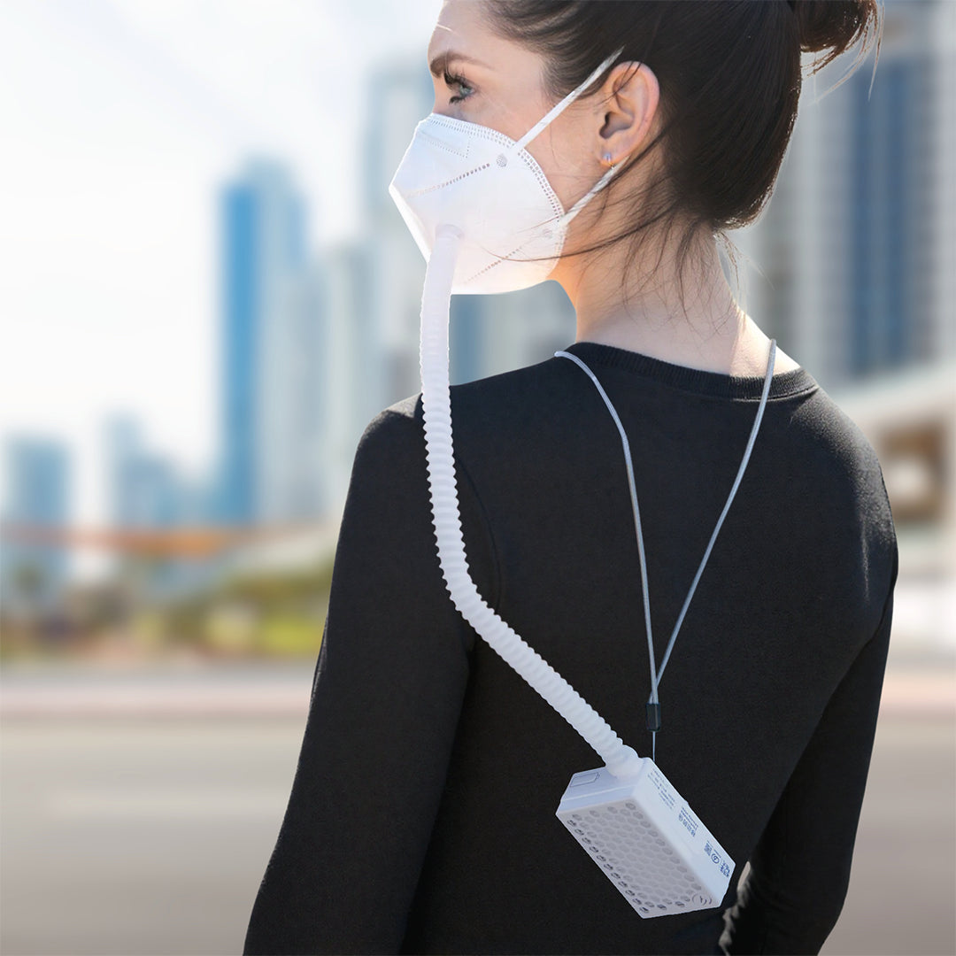 Person wearing a white face mask with a device attached, standing outdoors with blurred cityscape in the background.
