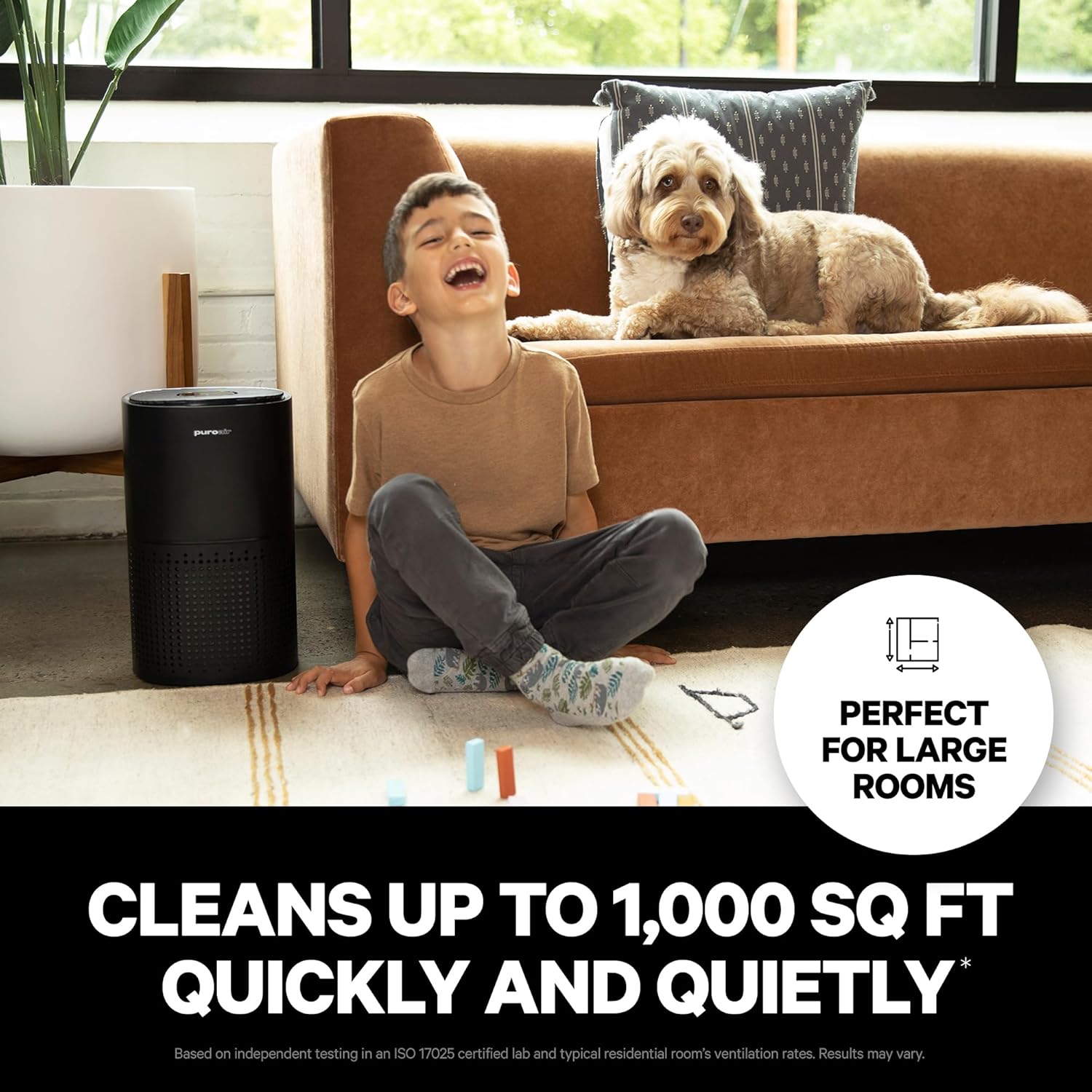 Child and dog sitting on a couch with a black air purifier in front, text indicating it cleans large rooms.